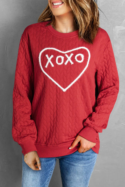 Woman wearing red quilted sweatshirt with white heart and XoXo text, paired with blue jeans