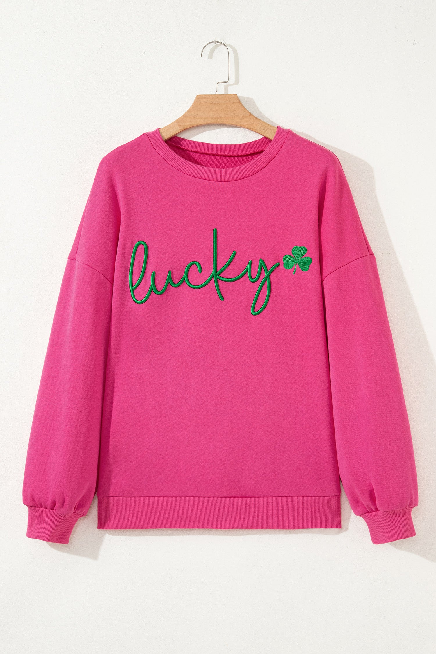 Pink sweatshirt with 'lucky' and a clover graphic on a hanger against a white background