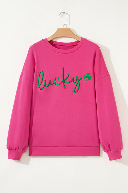 Pink sweatshirt with 'lucky' and a clover graphic on a hanger against a white background