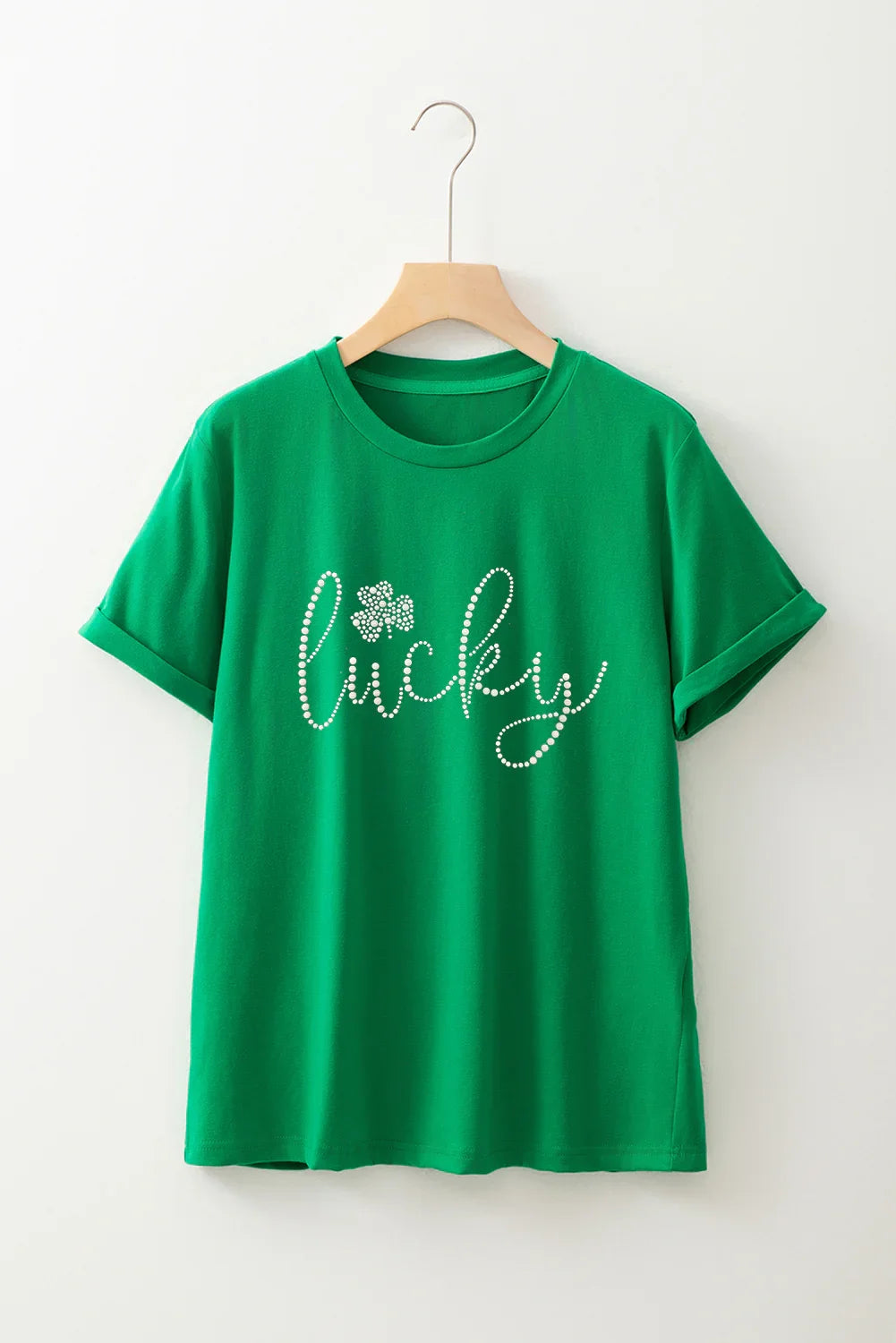 Green short-sleeve t-shirt with rolled cuffs hanging on wooden hanger, text 'lucky' with dotted design and clover