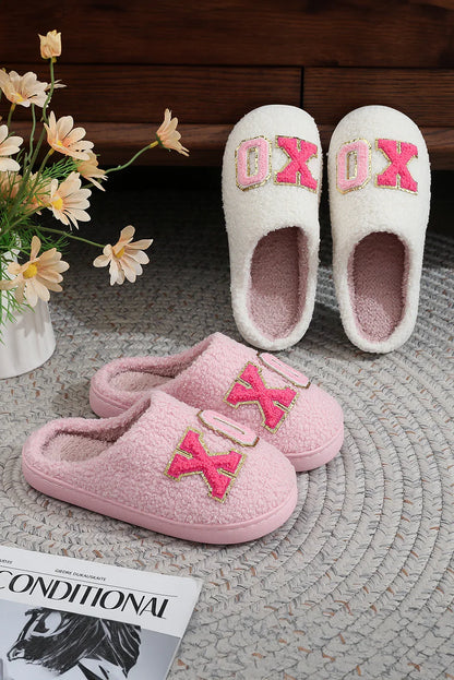 Cozy pink and white fleece slippers with XOXO design on a braided rug near flowers and magazine