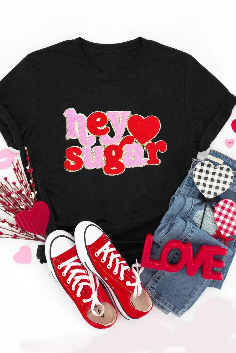 Black t-shirt with colorful hey sugar graphic, red sneakers, blue jeans, and Valentine's Day decor