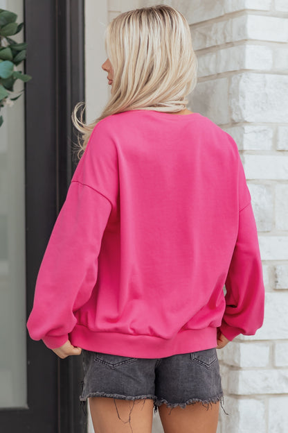 Person wearing a bright pink sweatshirt and denim shorts standing against a brick wall.