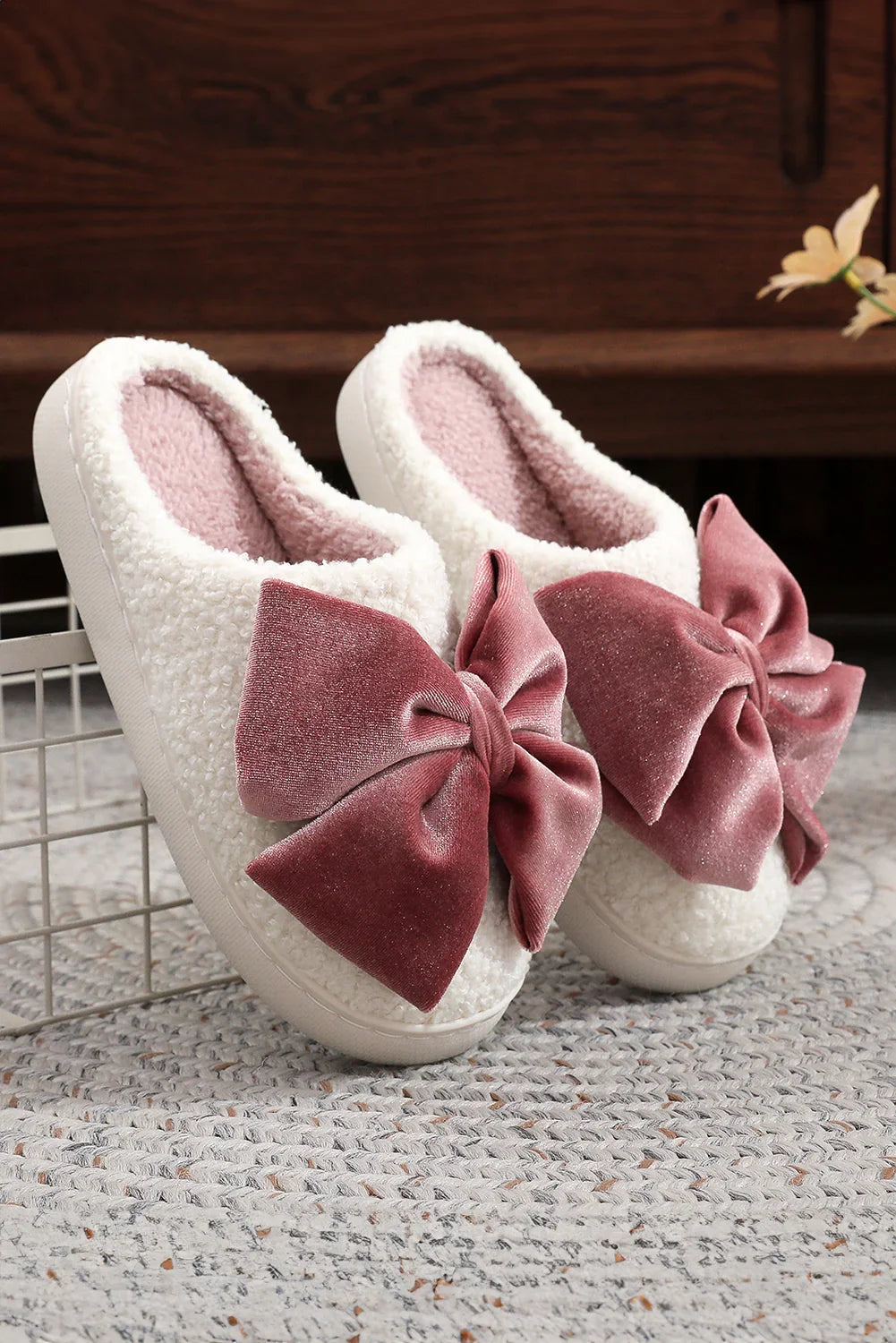 Cozy white fleece slippers with large soft pink velvet bows on woven rug