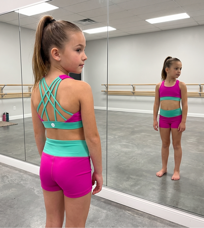a girl wearing horizon girls dancewear hot pink top with teal cross straps and bottoms in hot pink and teal accents.